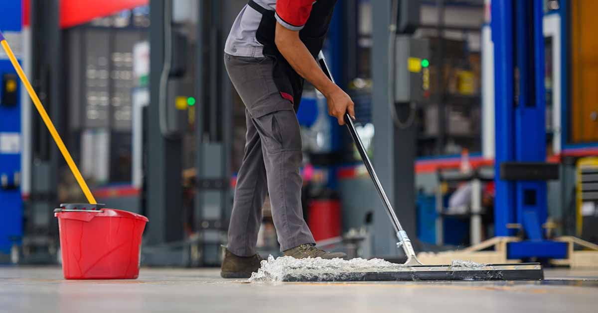 Car mechanic cleaning concrete floor